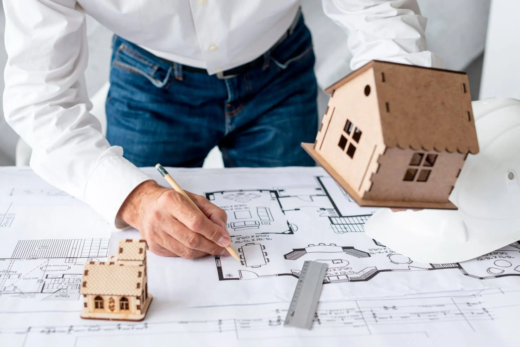 Person examining architectural plans with model houses and tools.