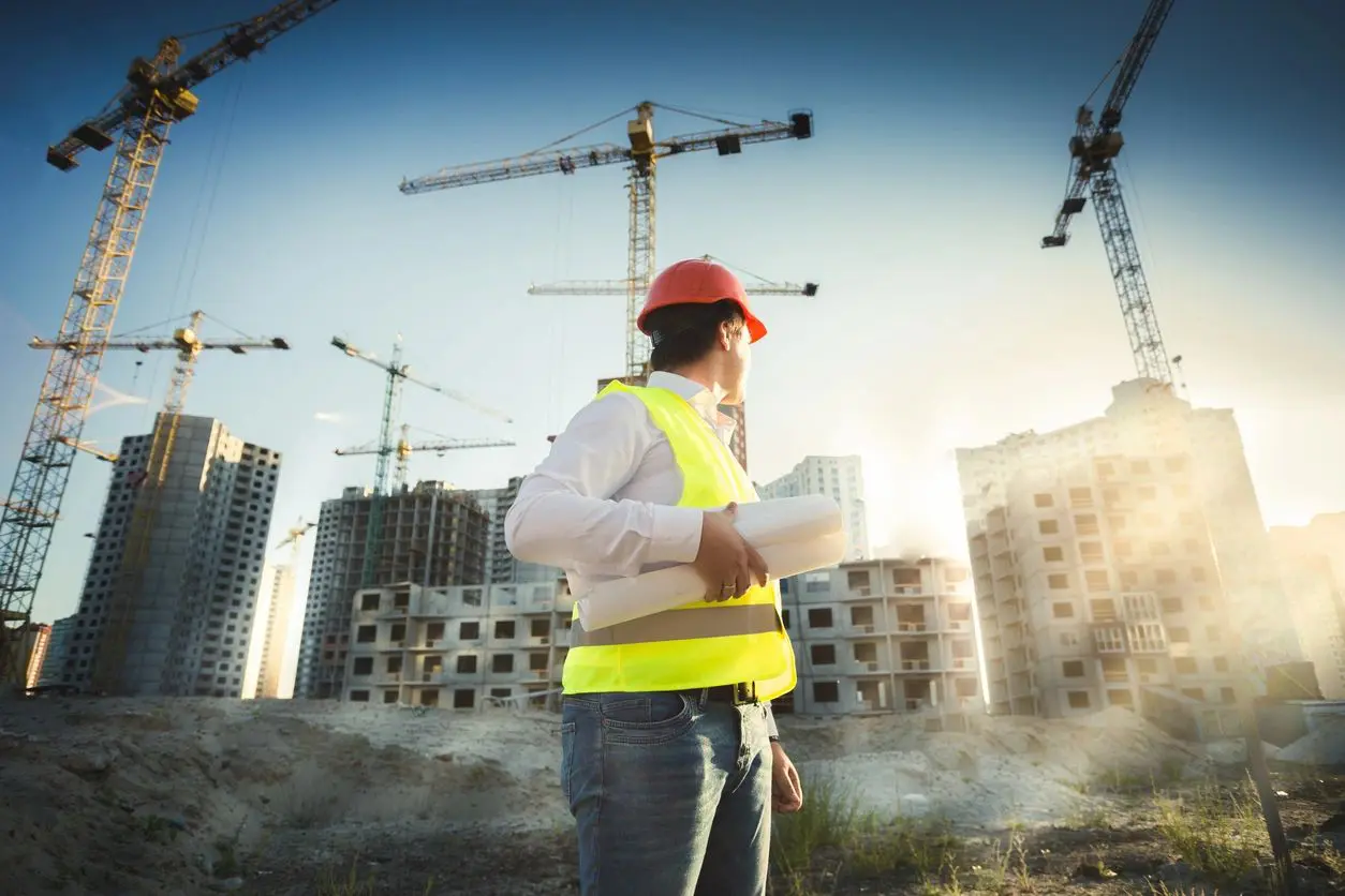 Construction worker in safety gear at a building site during sunset.