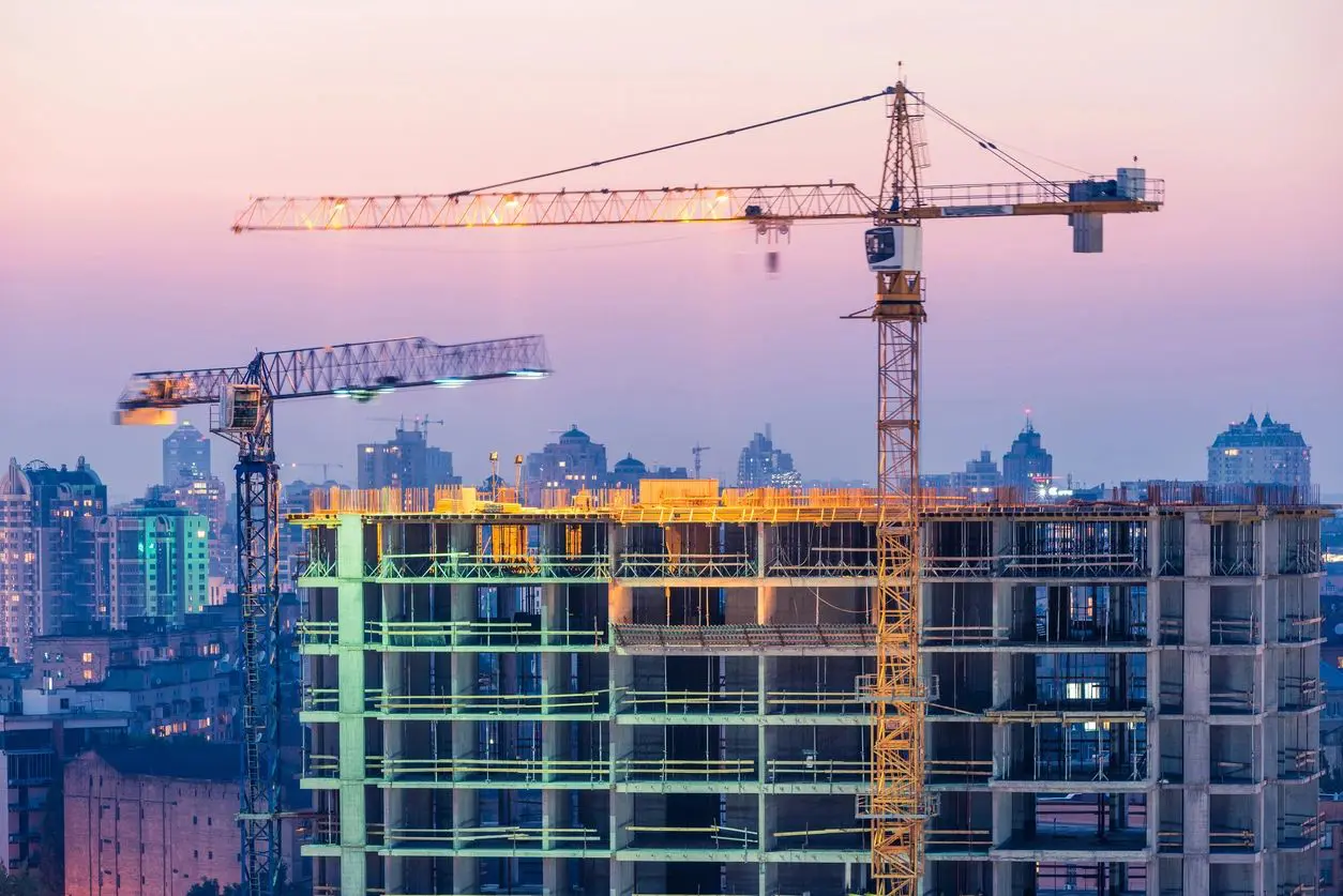 Construction cranes working on a building at sunset.