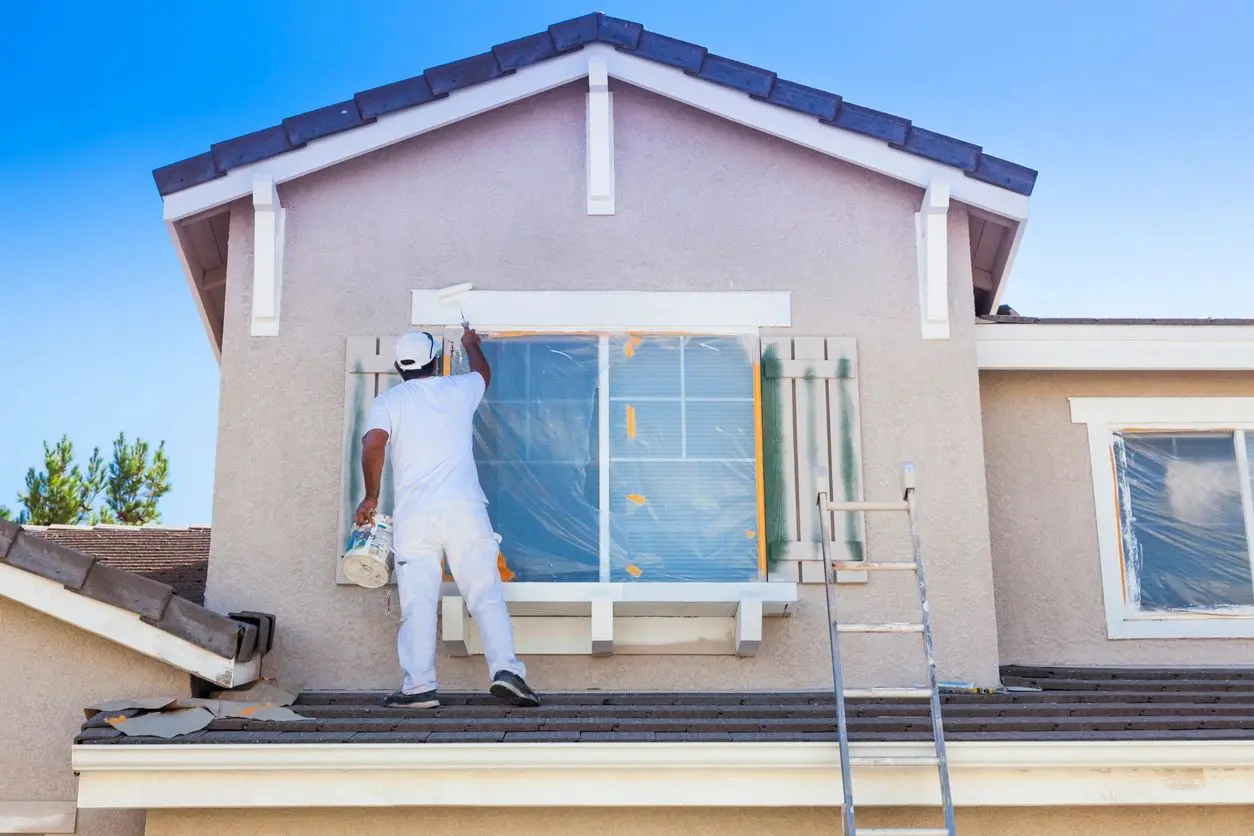 Painter working on a house exterior under a clear blue sky.