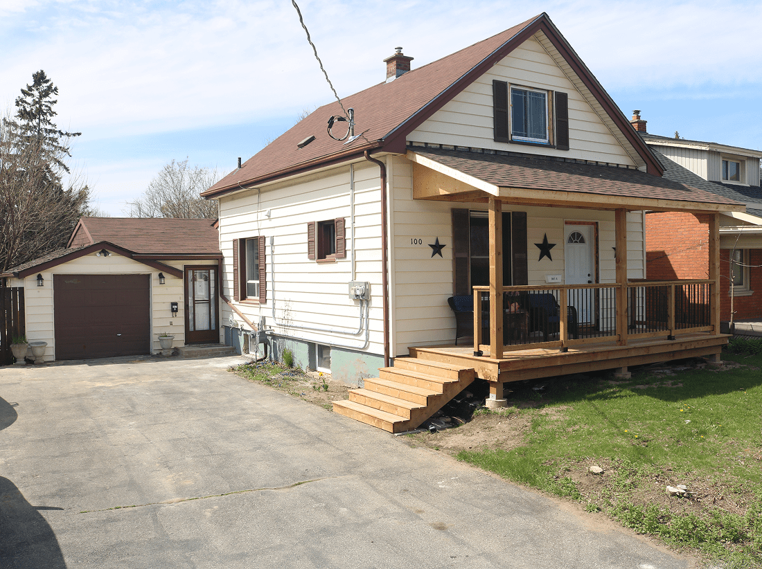 A small beige house with a sloped roof and a wooden porch.