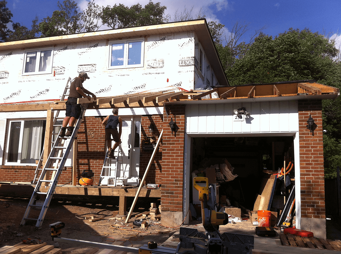 Workers renovating a house exterior with wooden beams and ladders.